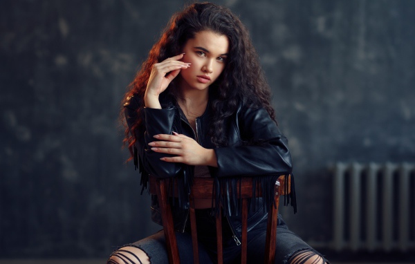 Модная красивая девушка в черное кожаной куртке сидит на стуле