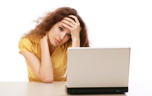 Грустная девушка сидит возле ноутбука 
