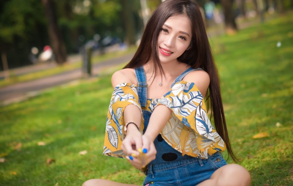 Улыбающаяся девушка азиатка сидит на траве