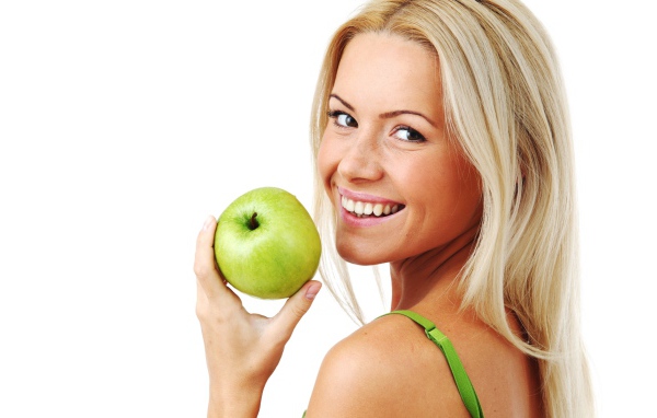 Улыбающаяся девушка блондинка с зеленым яблоком в руке на белом фоне