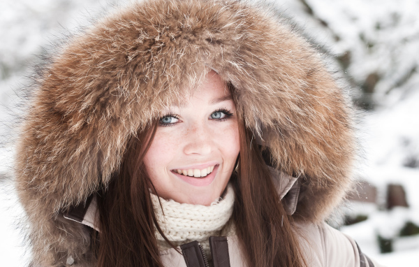 Улыбающаяся голубоглазая девушка в капюшоне зимой