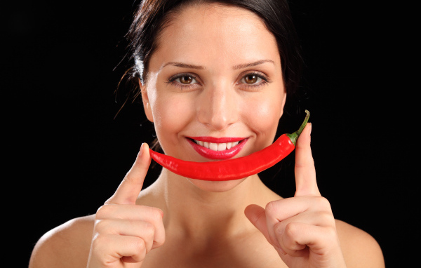 Улыбающаяся девушка с красным перцем на черном фоне