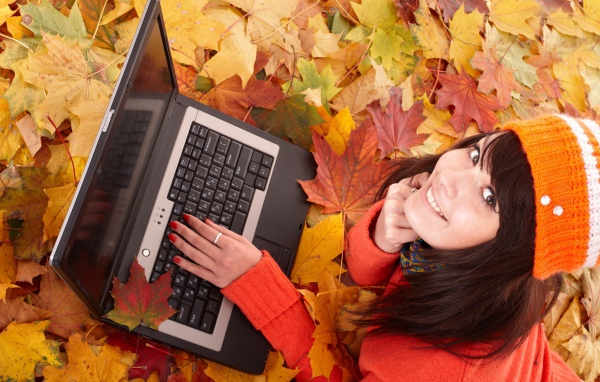 Девушка лежит на сухой опавшей листве с ноутбуком осенью