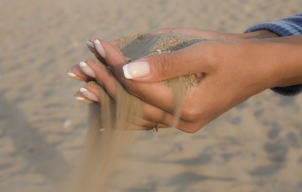 Желтый песок в руках у девушки с красивым маникюром