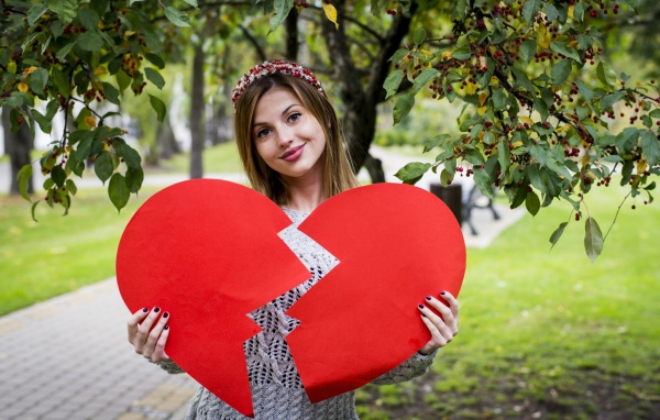 Молодая девушка с разбитым красным сердцем в руках