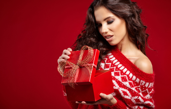 Beautiful brunette with a gift on a red background