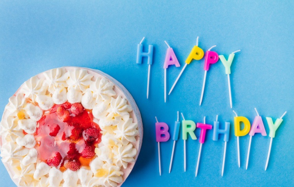 Красивый торт с кремом и клубникой на голубом фоне со свечами на день рождения