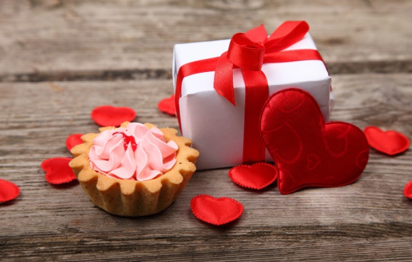 Пирожное, подарок и сердечки на деревянном фоне на День Святого Валентина