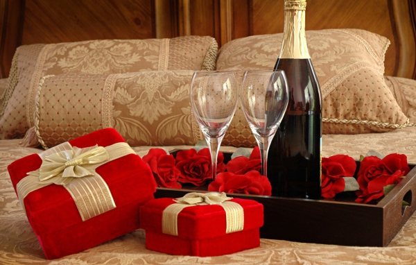 Бутылка вина, два бокала и подарки для романтического вечера на кровати 