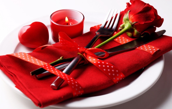 Роза, столовые приборы и зажженная свеча на белой тарелке 