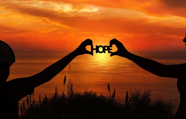 Силуэты пары держат в руках надпись HOPE на фоне заката