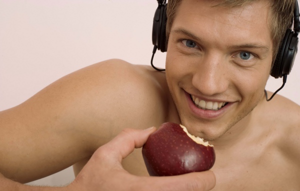 Красивый голубоглазый парень в наушниках с яблоком в руке