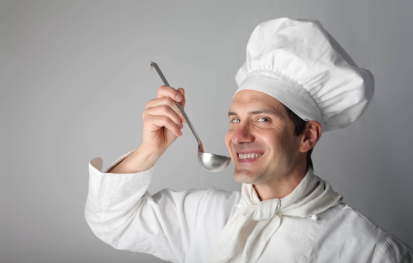 Улыбающийся мужчина повар с половником в руках на сером фоне