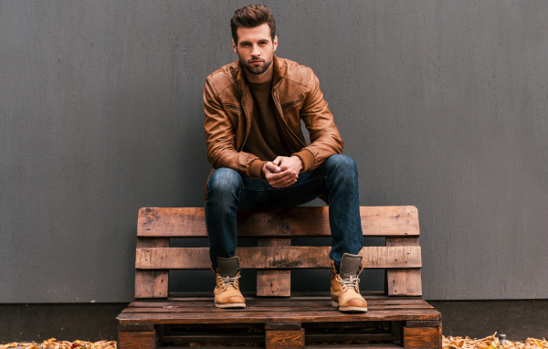 Молодой красивый мужчина сидит на деревянной лавке