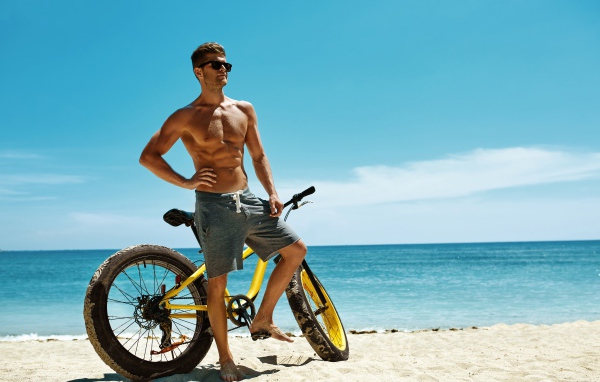 Молодой спортивный парень с велосипедом на пляже