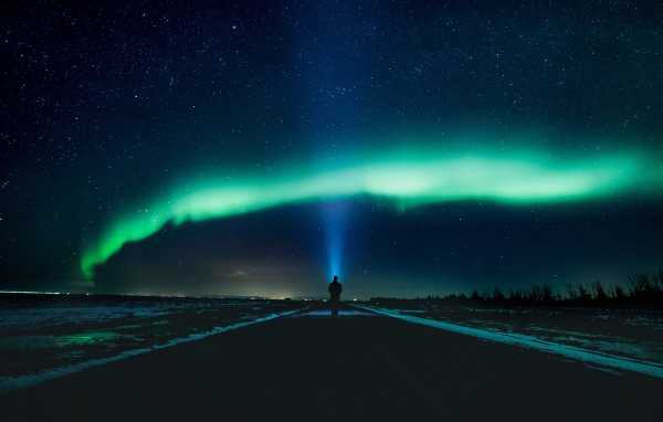 Человек идет по дороге ночью на фоне северного сияния
