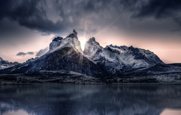 Рассвет солнца над горами у озера под пасмурным небом