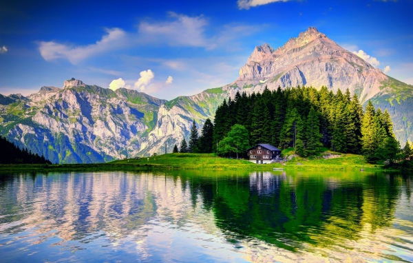 Лес и горы отражаются в озере под красивым голубым небом с белыми облаками