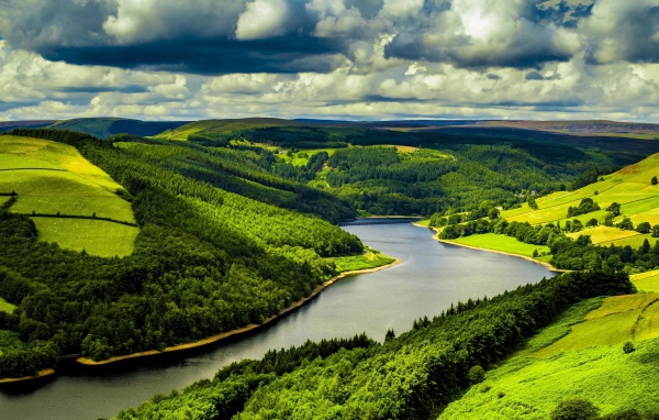 Зеленые холмы у реки под небом с густыми белыми облаками