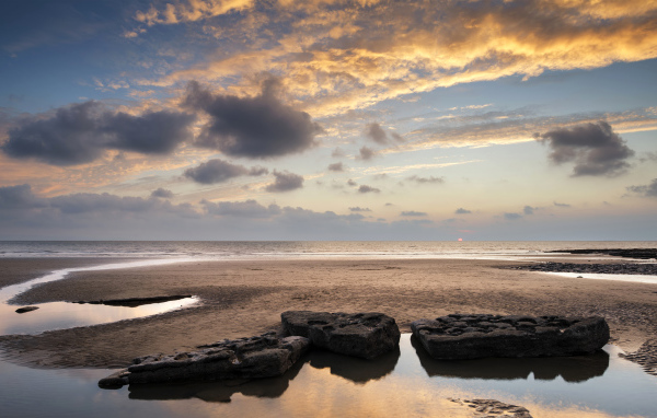 Большие камни в воде на песке под красивым небом