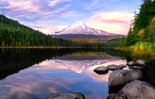 Заснеженная гора отражается в воде озера у зеленого леса