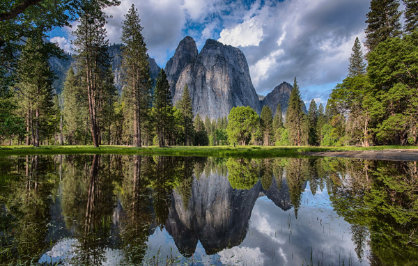 Каменные скалы и лес отражаются в воде 