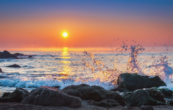 Волны бьются о камни на морском побережье на закате