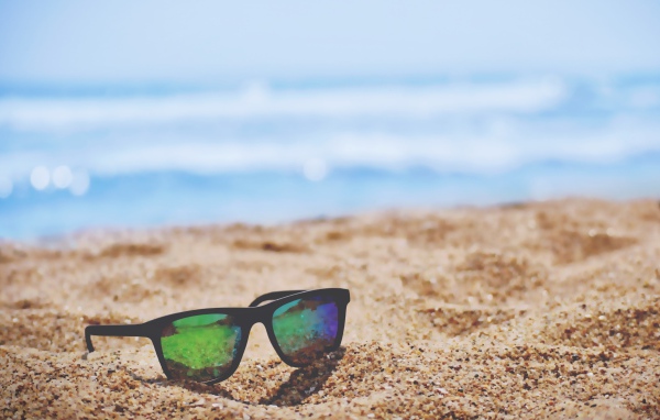 Солнцезащитные очки лежат на желтом песке у моря