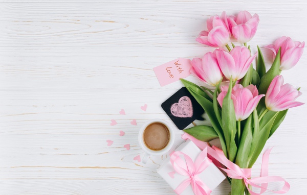 Букет розовых тюльпанов на столе с чашкой кофе и подарком 