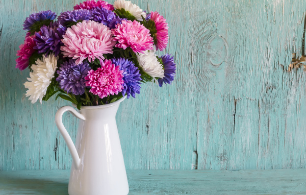 Разноцветные астры в вазе на деревянном фоне