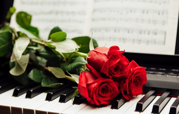 Три красные розы лежат на клавишах пианино с нотами