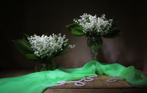 Два букета ландышей с бусами на столе 