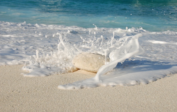 Белые морские волны бьются об камень на желтом песке