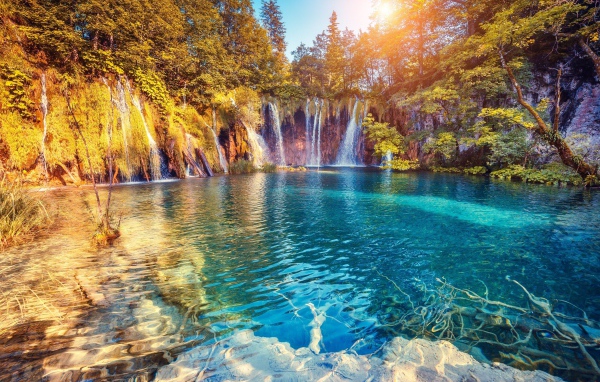 Водопад в лучах солнца стекает со скалы в реку