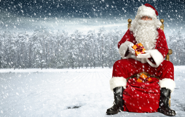 Веселый Санта Клаус сидит на мешке в заснеженном лесу