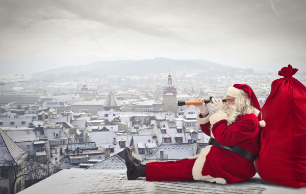 Санта Клаус сидит на крыше дома с большим красным мешком