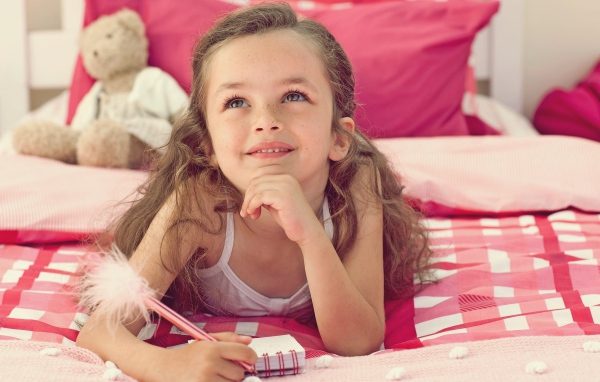 Замечтавшаяся маленькая девочка лежит на кровати