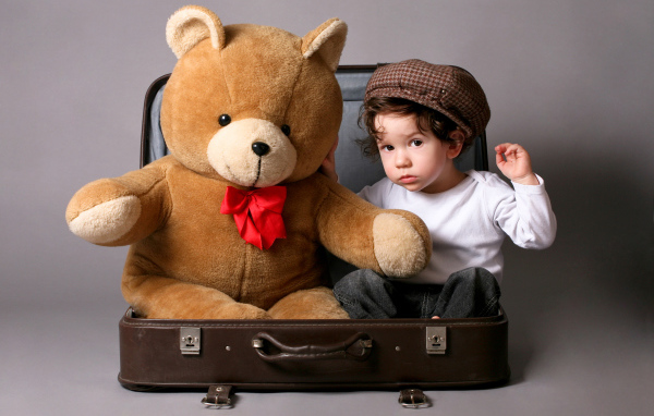 Маленький мальчик сидит в чемодане с плюшевым мишкой 