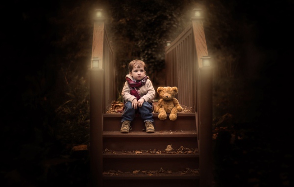 Маленький мальчик сидит с игрушечным мишкой на ступеньках