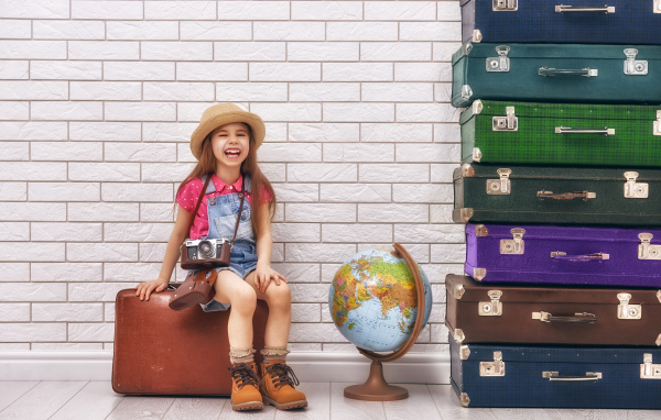 Маленькая девочка с фотоаппаратом сидит на чемодане