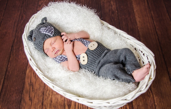 Спящий младенец в сером костюме в белой корзине