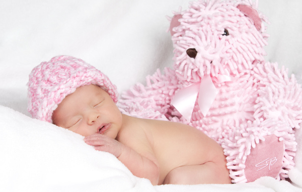 Спящий грудной ребенок в шапке с большим розовым медведем