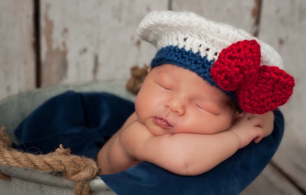 Спящий грудной ребенок в вязаной шапочке с красным бантом
