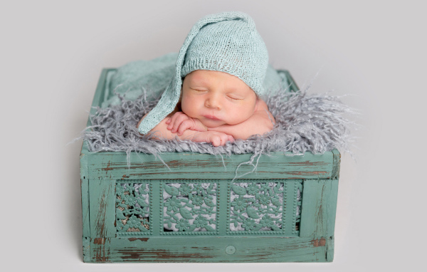 Спящий ребенок в зеленом ящике на сером фоне