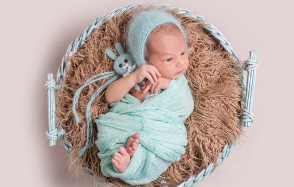 Маленький ребенок в корзине на сером фоне