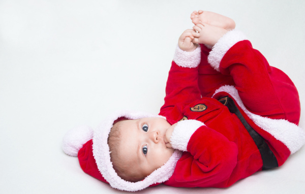 Маленький ребенок в красном новогоднем костюме на сером фоне