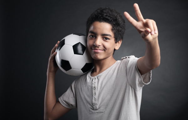 Мальчик с футбольным мячом на плече на сером фоне