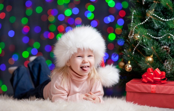 Смешная девочка в новогодней шапке у елки