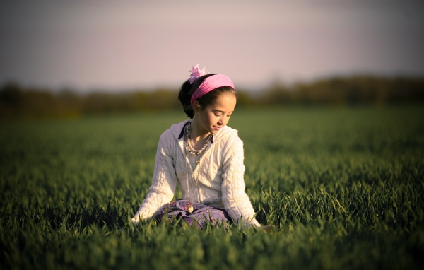 Девочка с розовой повязкой на голове сидит в зеленой траве