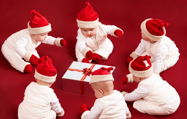 Младенцы в новогодних костюмах с подарком на красном фоне